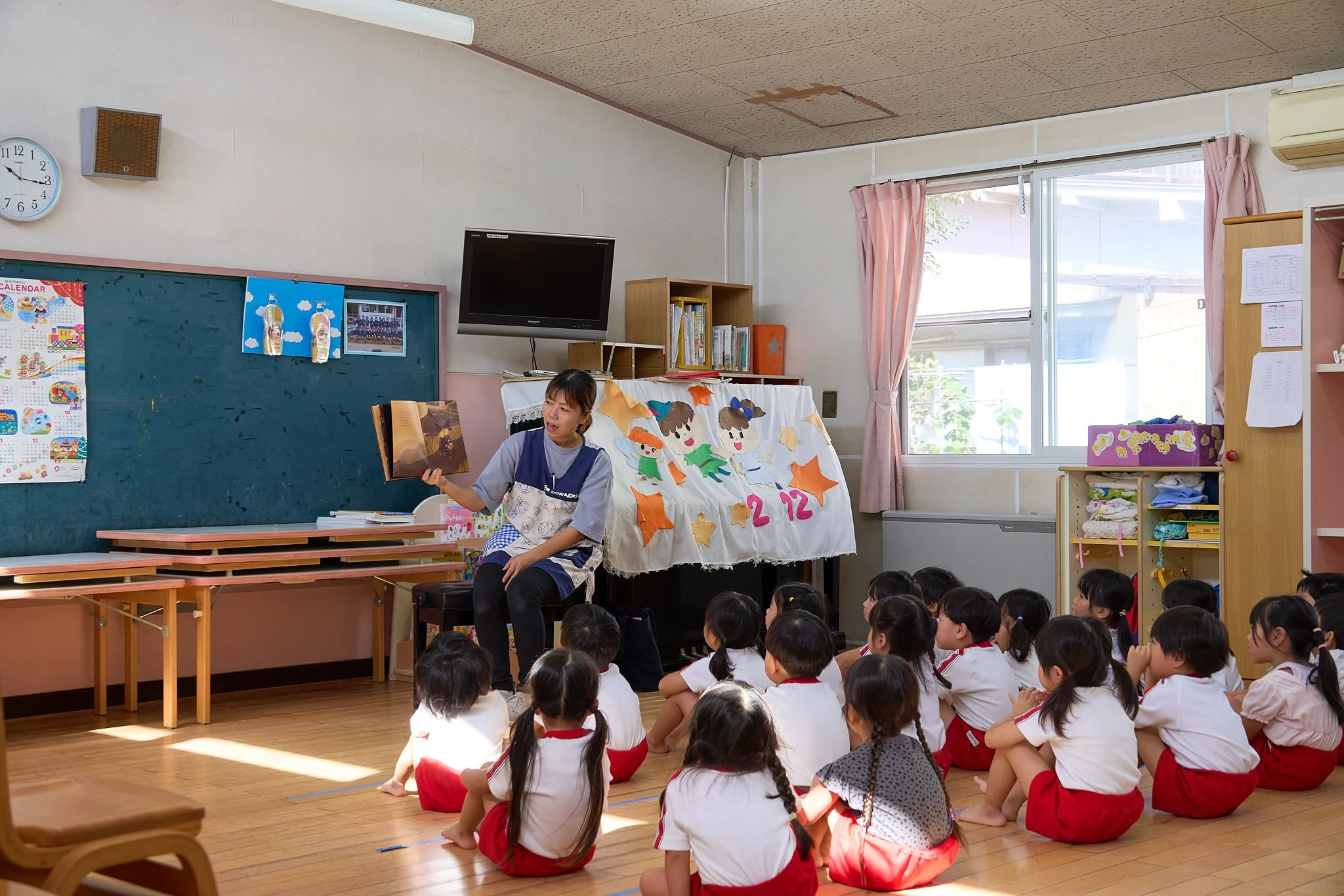 保育士が絵本を読み、園児が座って聞いている様子